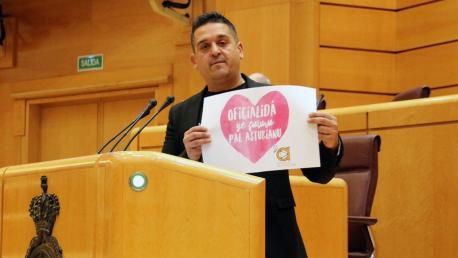 Carles Mulet nel Senáu con cartelu Iniciativa pol Asturianu